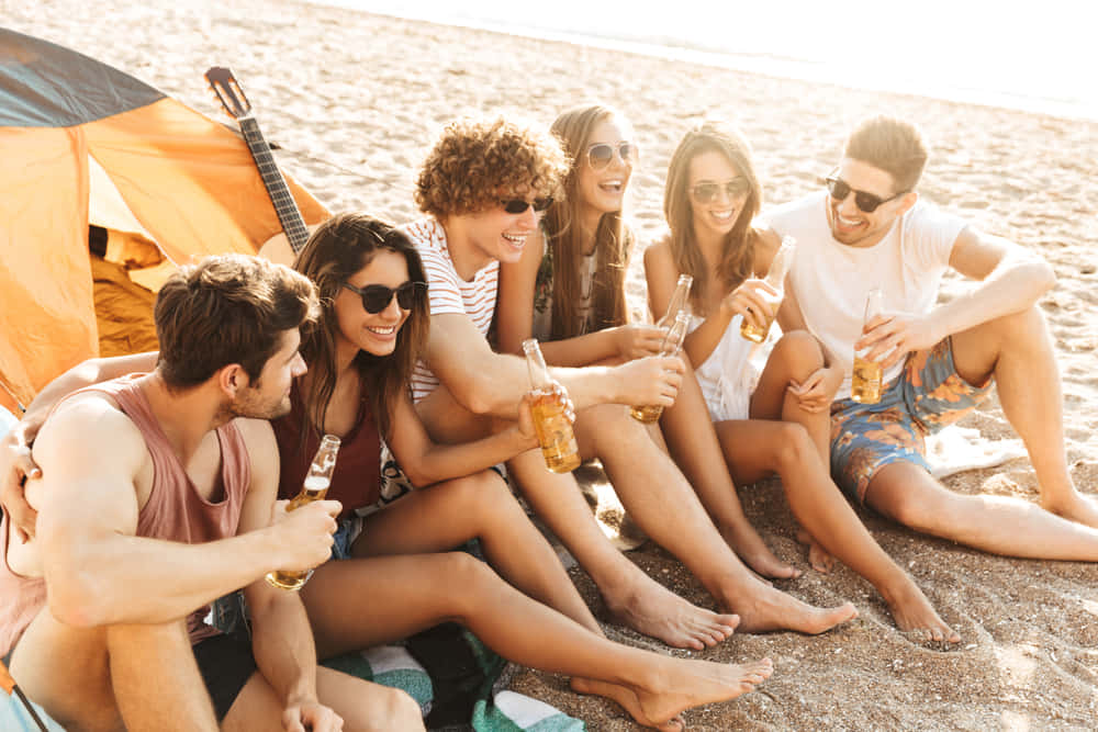 Group of cheerful happy friends camping at the beach, drinking beer